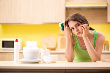 Genç bir kadın mutfakta bulaşık yıkıyor.