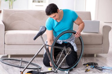 Evde bisiklet tamir eden genç bir adam.