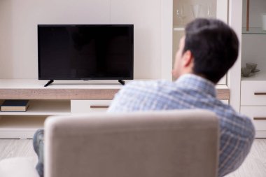 Genç adam evde televizyon izliyor.