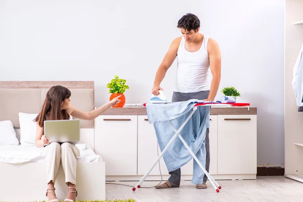 Hombre planchando, su perezosa esposa sentada — Foto de Stock