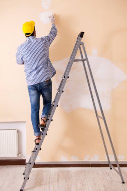 Genç müteahhit zımpara kağıdıyla duvarı zımparalıyor. 