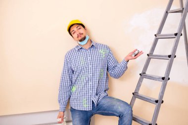 Genç müteahhit zımpara kağıdıyla duvarı zımparalıyor. 