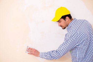 Genç müteahhit zımpara kağıdıyla duvarı zımparalıyor. 