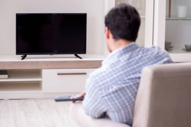 Genç adam evde televizyon izliyor.