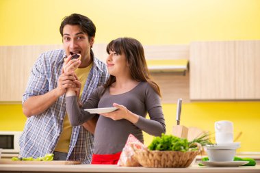 Man and pregnant woman preparing salad in kitchen  clipart