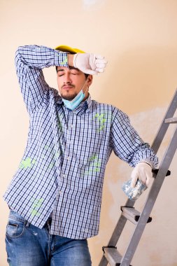 Genç müteahhit zımpara kağıdıyla duvarı zımparalıyor. 