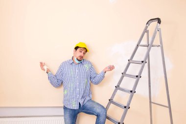 Genç müteahhit zımpara kağıdıyla duvarı zımparalıyor. 