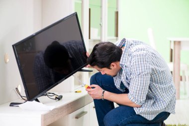Genç adam evde televizyon tamir ediyor. 