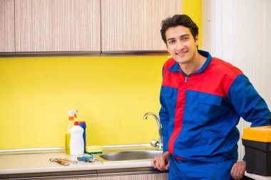 Tesisatçı mutfakta musluğu tamir ediyor.