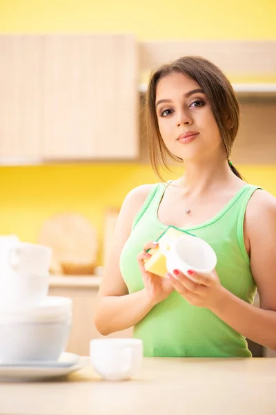 Mladá žena čištění a mytí nádobí v kuchyni — Stock fotografie