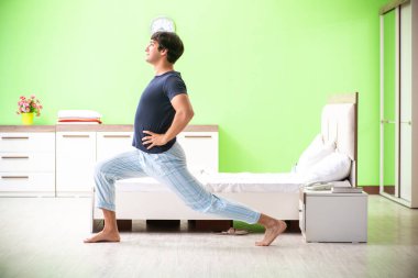 Pijamalı genç adam sabah egzersizi yapıyor. 