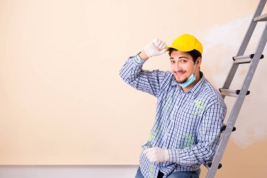 Genç müteahhit zımpara kağıdıyla duvarı zımparalıyor. 