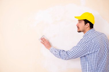 Genç müteahhit zımpara kağıdıyla duvarı zımparalıyor. 