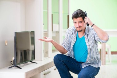 Genç adam evde televizyon tamir ediyor. 