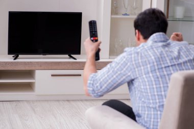 Genç adam evde televizyon izliyor.
