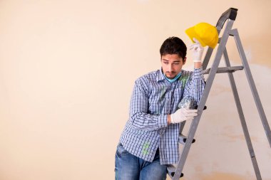 Genç müteahhit zımpara kağıdıyla duvarı zımparalıyor. 