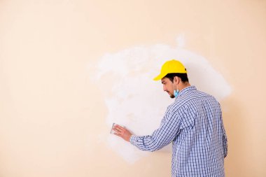 Genç müteahhit zımpara kağıdıyla duvarı zımparalıyor. 
