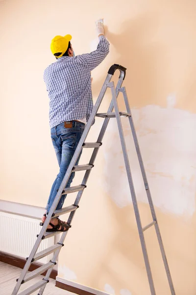 Jovem empreiteiro lixar parede para baixo com lixa — Fotografia de Stock