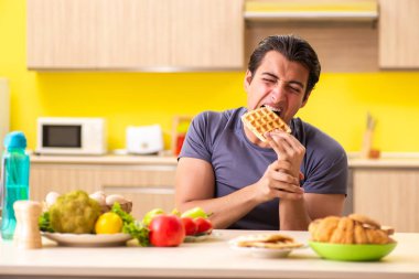 Sağlıklı ve sağlıksız yemek arasında zor bir seçim yapan bir adam.