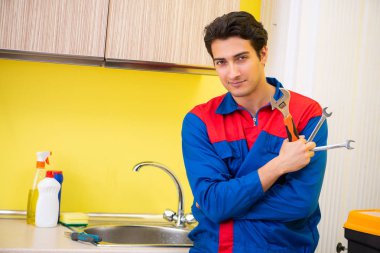 Tesisatçı mutfakta musluğu tamir ediyor.