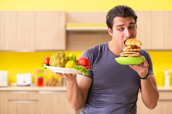 Hombre que tiene difícil elección entre la comida sana y no saludable —  Fotos de Stock