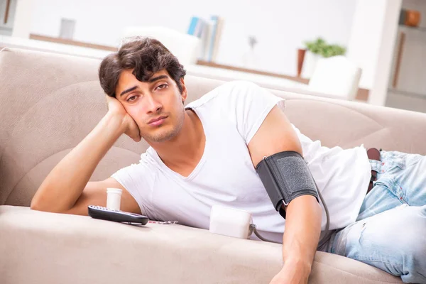 Hombre joven midiendo la presión arterial en casa — Foto de Stock