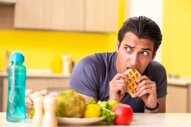 Sağlıklı ve sağlıksız yemek arasında zor bir seçim yapan bir adam.