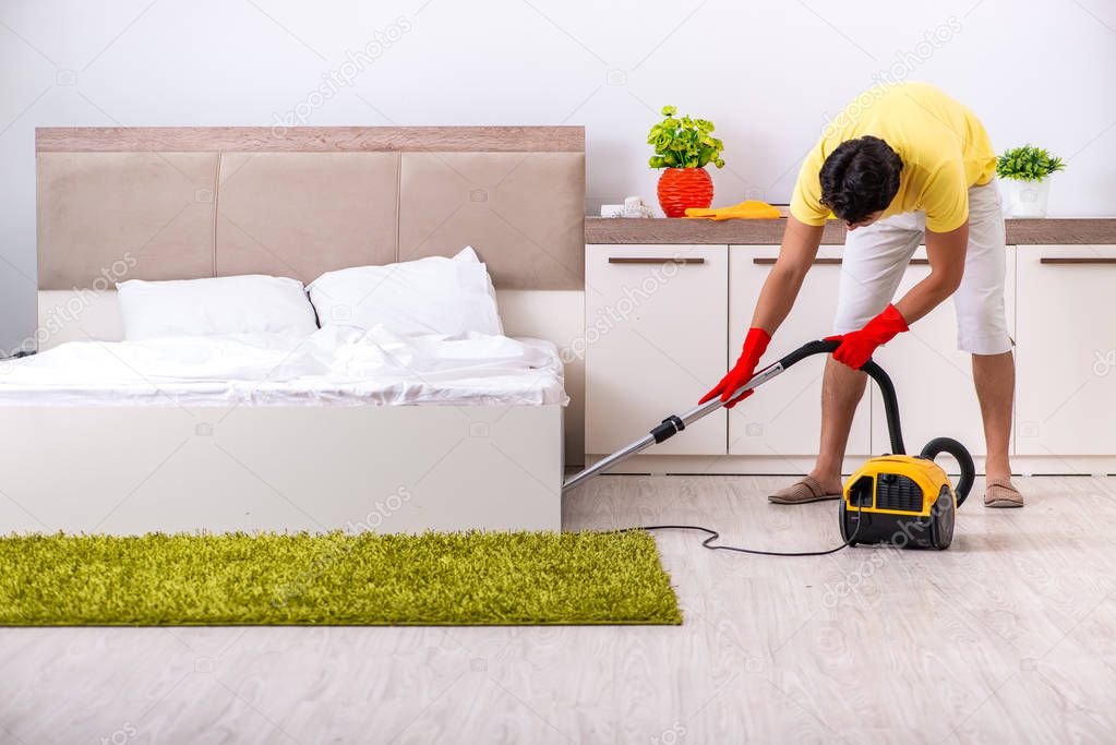Young handsome man cleaning in the bedroom