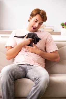 Genç adam evde kedi yavrusuyla oynuyor.