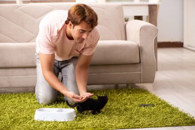 Genç adam evde kedi yavrusuyla oynuyor.