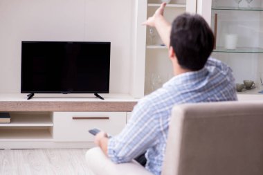 Genç adam evde televizyon izliyor.