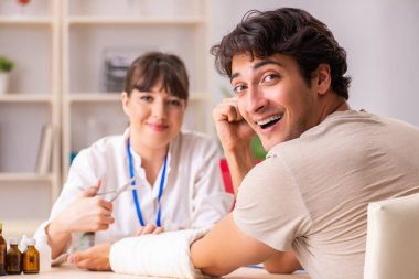 Kolu bandajlı genç adam kadın doktor travmatologunu ziyaret ediyor.