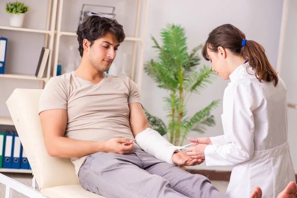 Hombre joven con el brazo vendado visitando a la doctora traumatologis — Foto de Stock