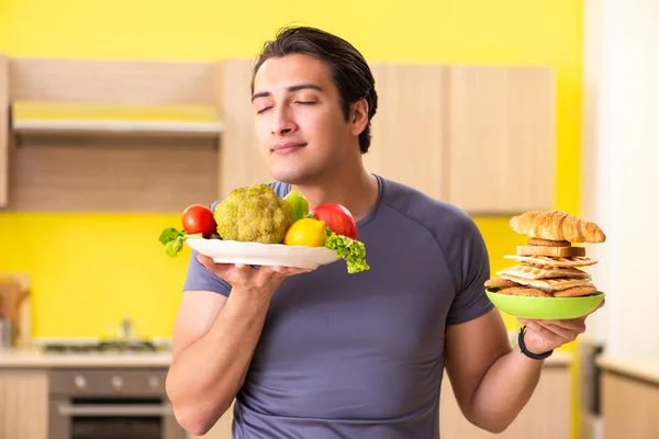 Homem tendo escolha difícil entre alimentos saudáveis e não saudáveis — Fotografia de Stock