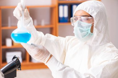 Laboratuvarda çalışan koruyucu elbise giyen genç bir biyokimyacı.