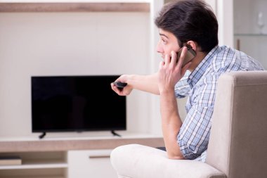 Genç adam evde televizyon izliyor.
