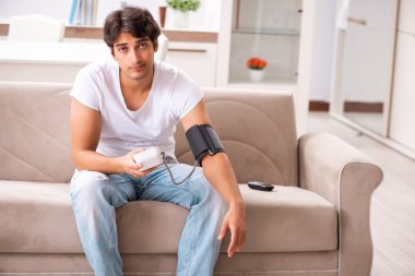 Evde kan basıncını ölçen genç bir adam.