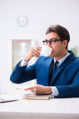 Genç yakışıklı işadamı ofiste kahve içiyor. 