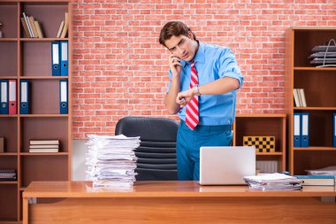 Ofiste aşırı işi olan genç bir çalışan oturuyor. 