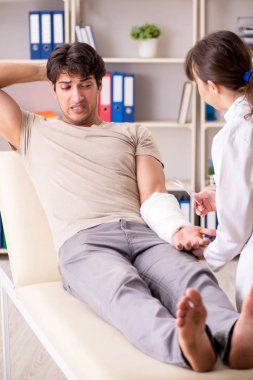 Kolu bandajlı genç adam kadın doktor travmatologunu ziyaret ediyor.