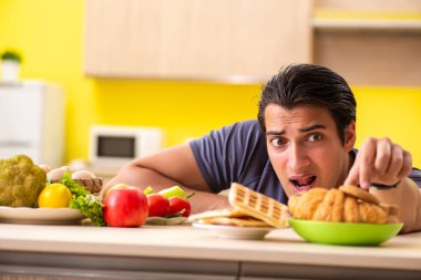 Sağlıklı ve sağlıksız yemek arasında zor bir seçim yapan bir adam.