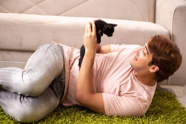 Genç adam evde kedi yavrusuyla oynuyor.