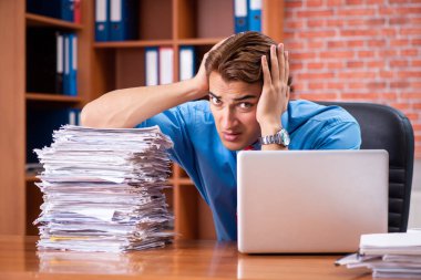 Ofiste aşırı işi olan genç bir çalışan oturuyor. 