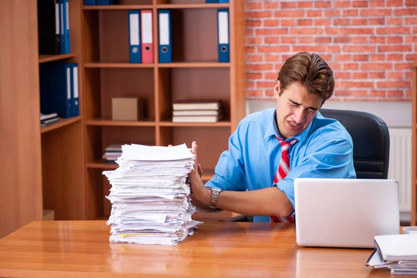 Jovem funcionário com excesso de trabalho sentado no escritório — Fotografia de Stock