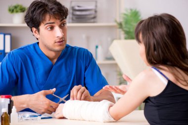 Kolu bandajlı genç kadın erkek doktor traumotologis 'i ziyaret ediyor.