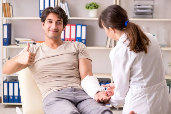 Hombre joven con el brazo vendado visitando a la doctora traumatologis — Foto de Stock