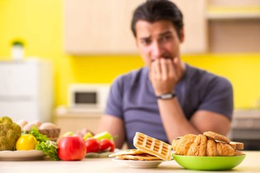Sağlıklı ve sağlıksız yemek arasında zor bir seçim yapan bir adam.