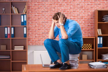 Ofiste aşırı işi olan genç bir çalışan oturuyor. 