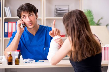 Kolu bandajlı genç bir kadın erkek doktor traumotoloğu ziyaret ediyor. 