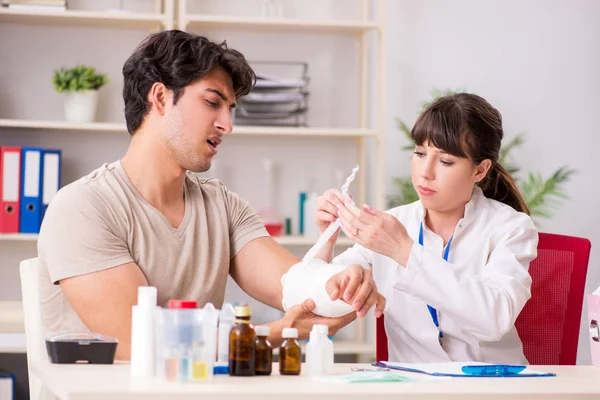 Young man with bandaged arm visiting female doctor traumatologis — Stock Photo, Image